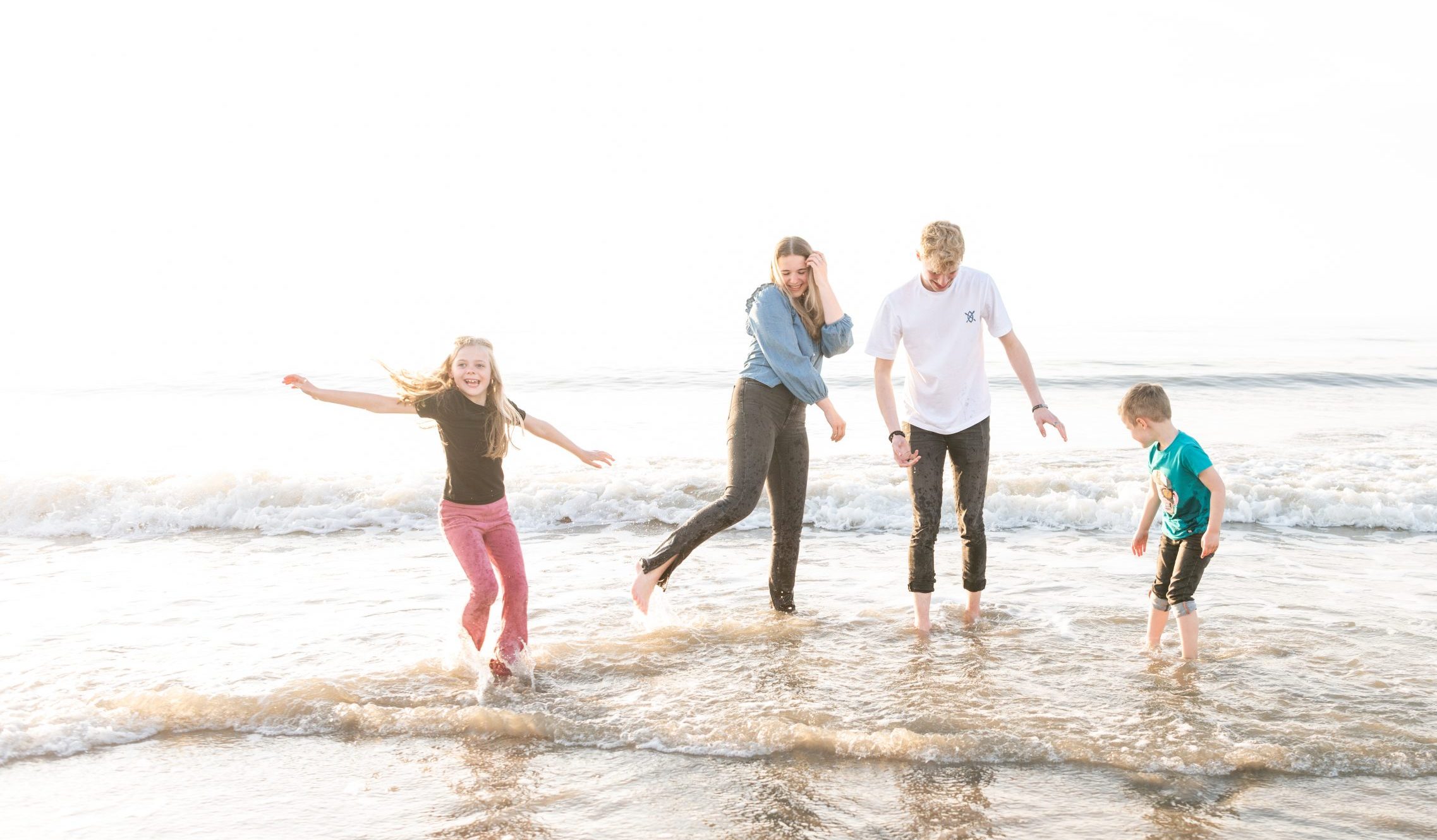 Familie fotoshoot aan zee: kinderen en ouders spelen in de branding