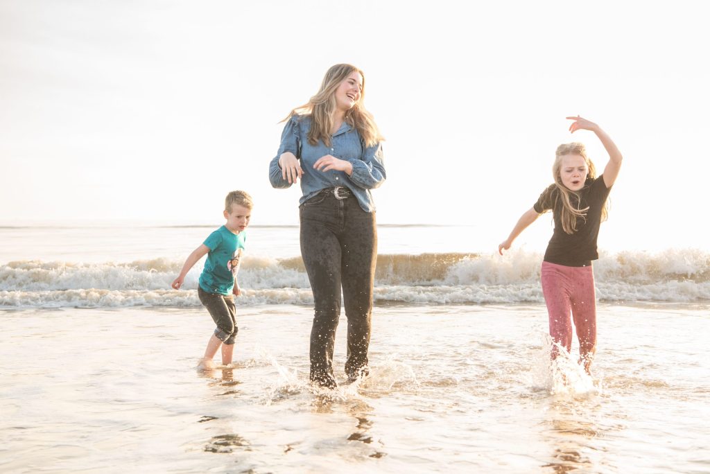 Moeder en kinderen springen door de golven aan het strand