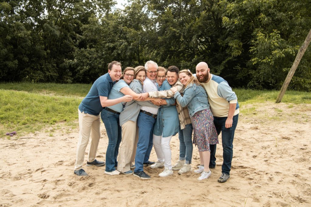 Grote familie lacht en knuffelt elkaar op een zandvlakte