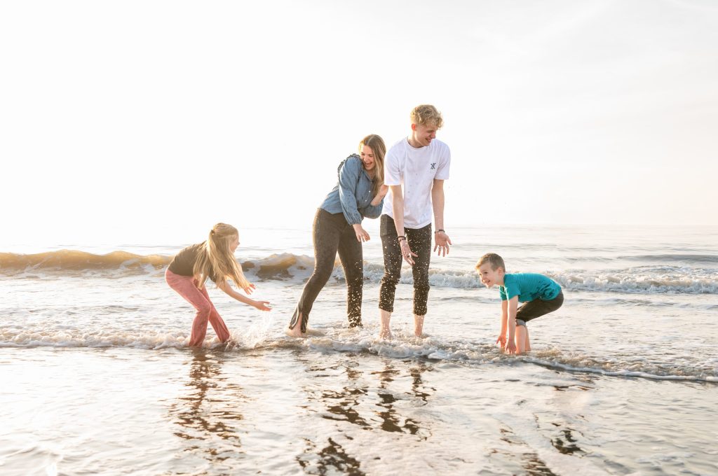 Gezin met tieners speelt in de zee tijdens een familieshoot aan het strand